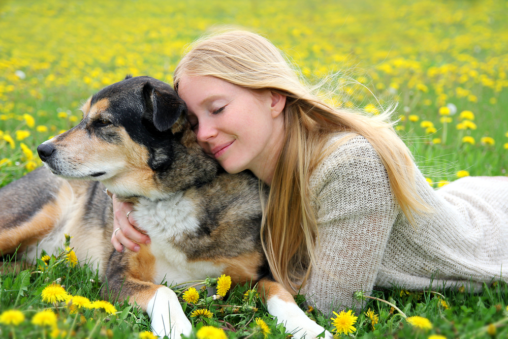 Girl lying in the grass tenderly hugging her pet, reflecting the bond between owners and animals